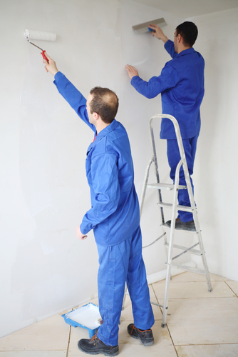 two men paint and working on the same wall