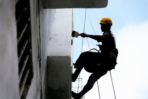 painting the exterior of a building hanging from cabels